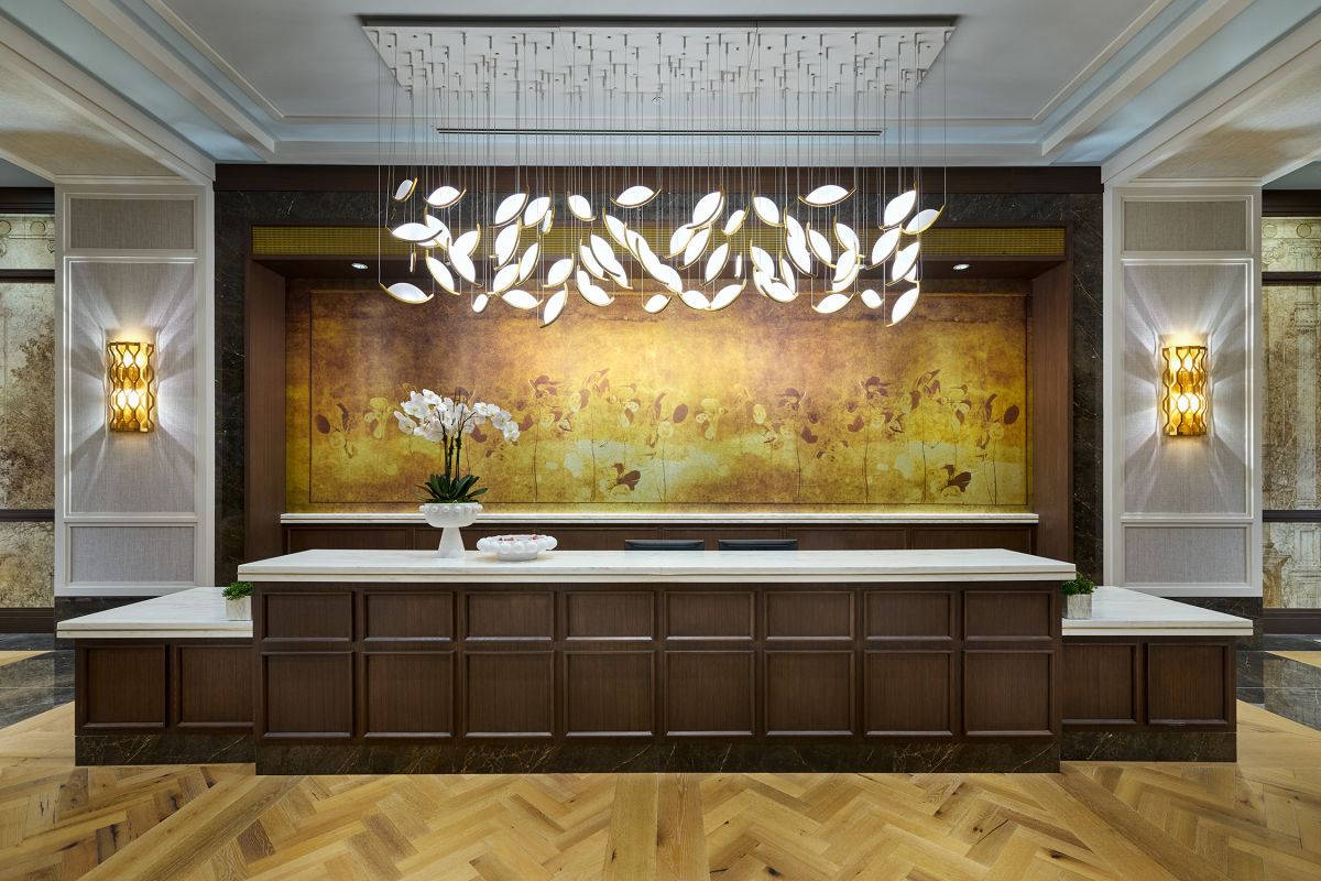 Modern hotel reception desk at Hanover Buffalo Bayou, featuring an ornate chandelier, flower arrangement, and golden accent wall.