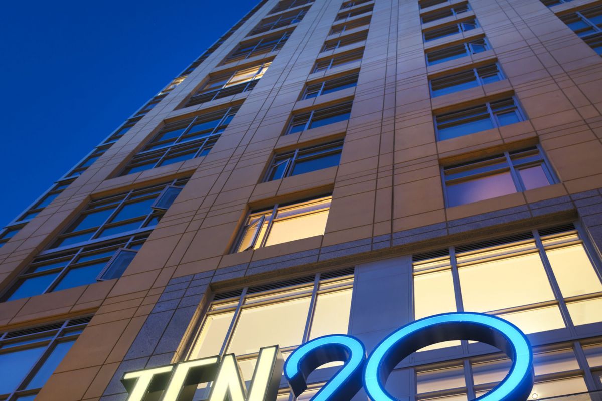 Tall building at dusk with illuminated "TEN 20" sign at the entrance, viewed from a low angle.