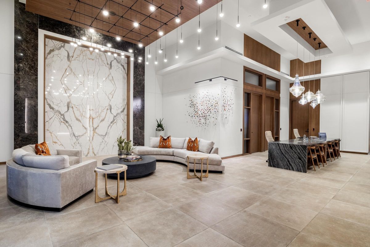 Modern lounge with elegant lighting, beige sofas, marble wall art, and a dining table with hanging pendant lights.