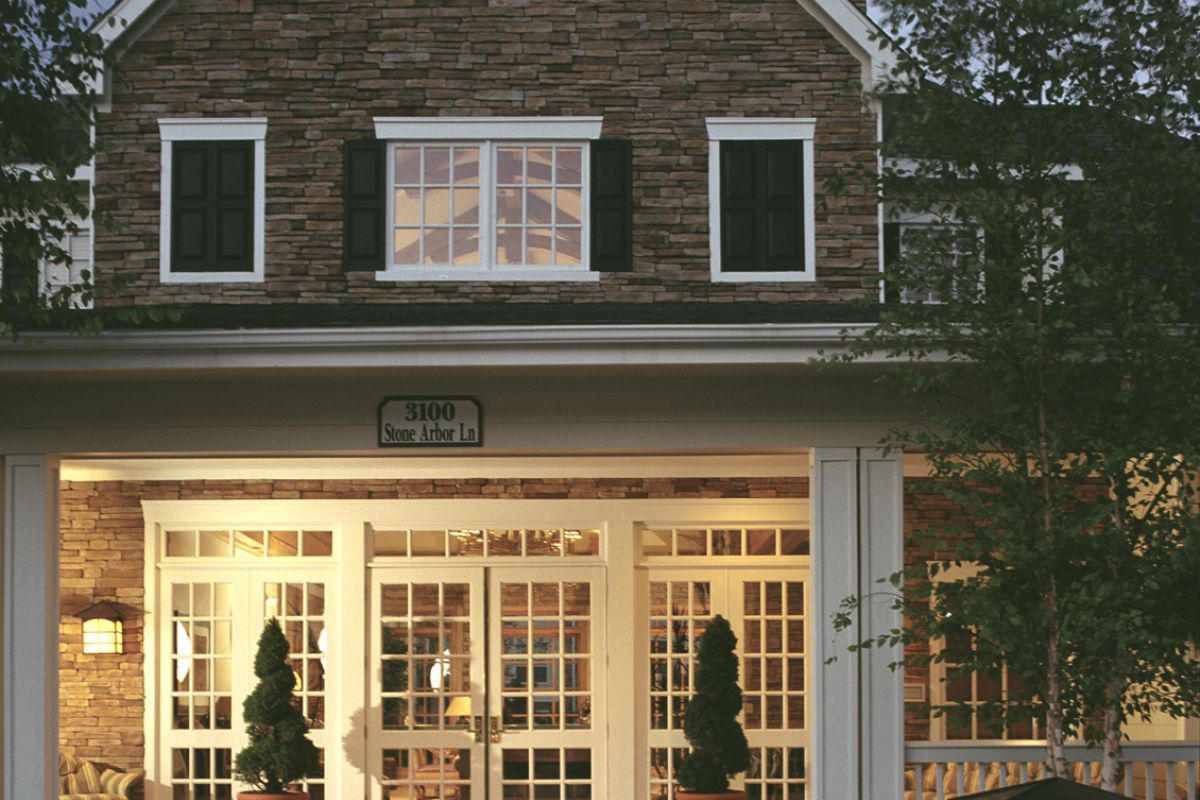 Front view of a cozy building with large windows, potted plants, and a stone well at dusk.