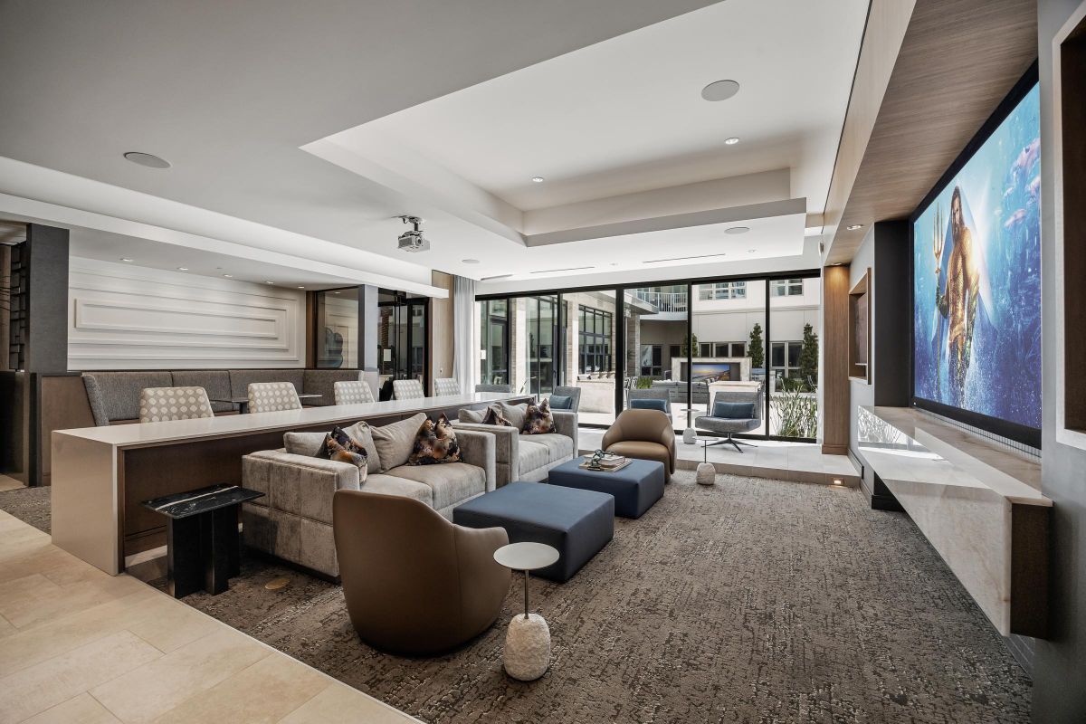 Hanover Laguna Niguel Modern home theater with gray sofas, brown chairs, a large screen displaying a movie, and ample natural light.