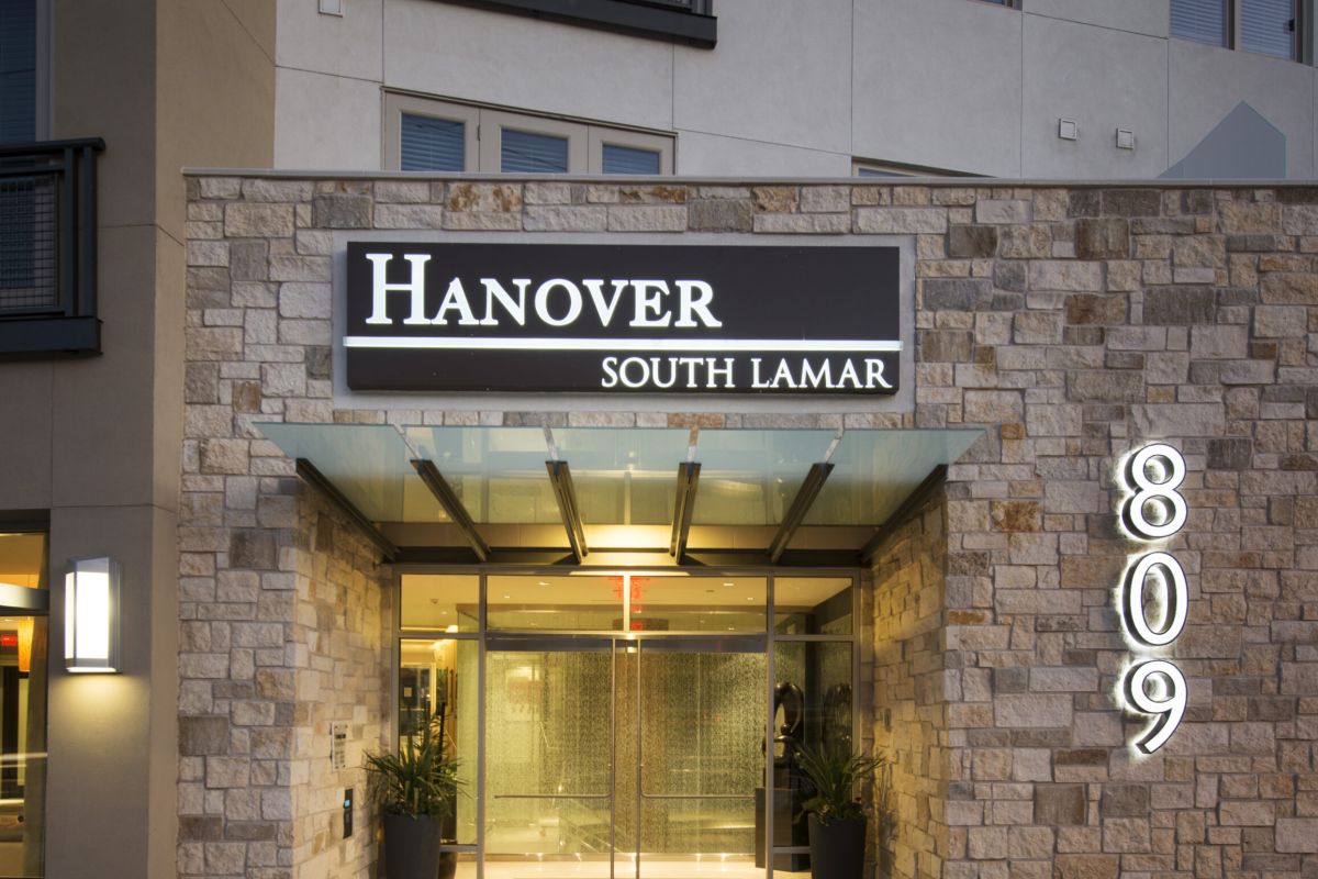 Glass entrance of Hanover South Lamar building with stone walls and illuminated address number 809.