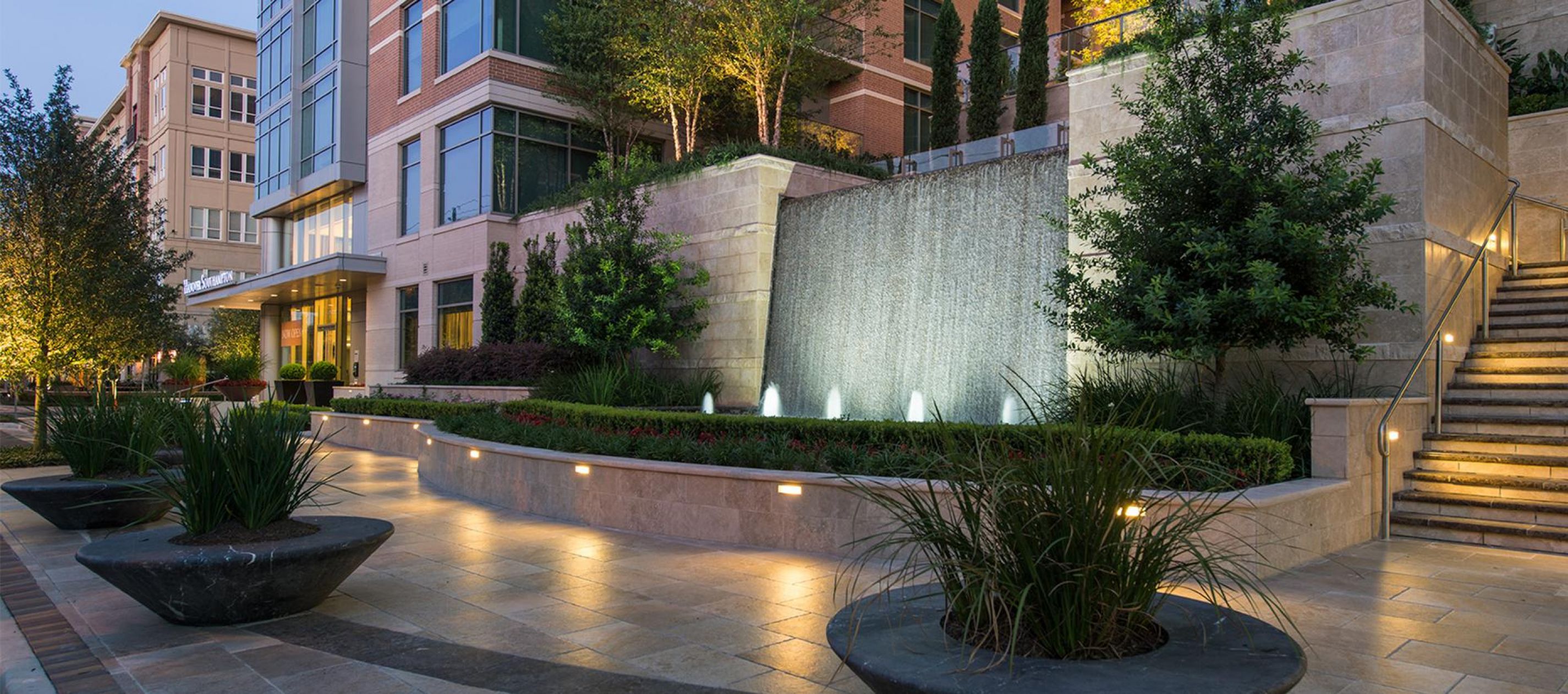 Hanover Company Modern building with an illuminated waterfall, lush greenery, and steps leading up to the entrance.