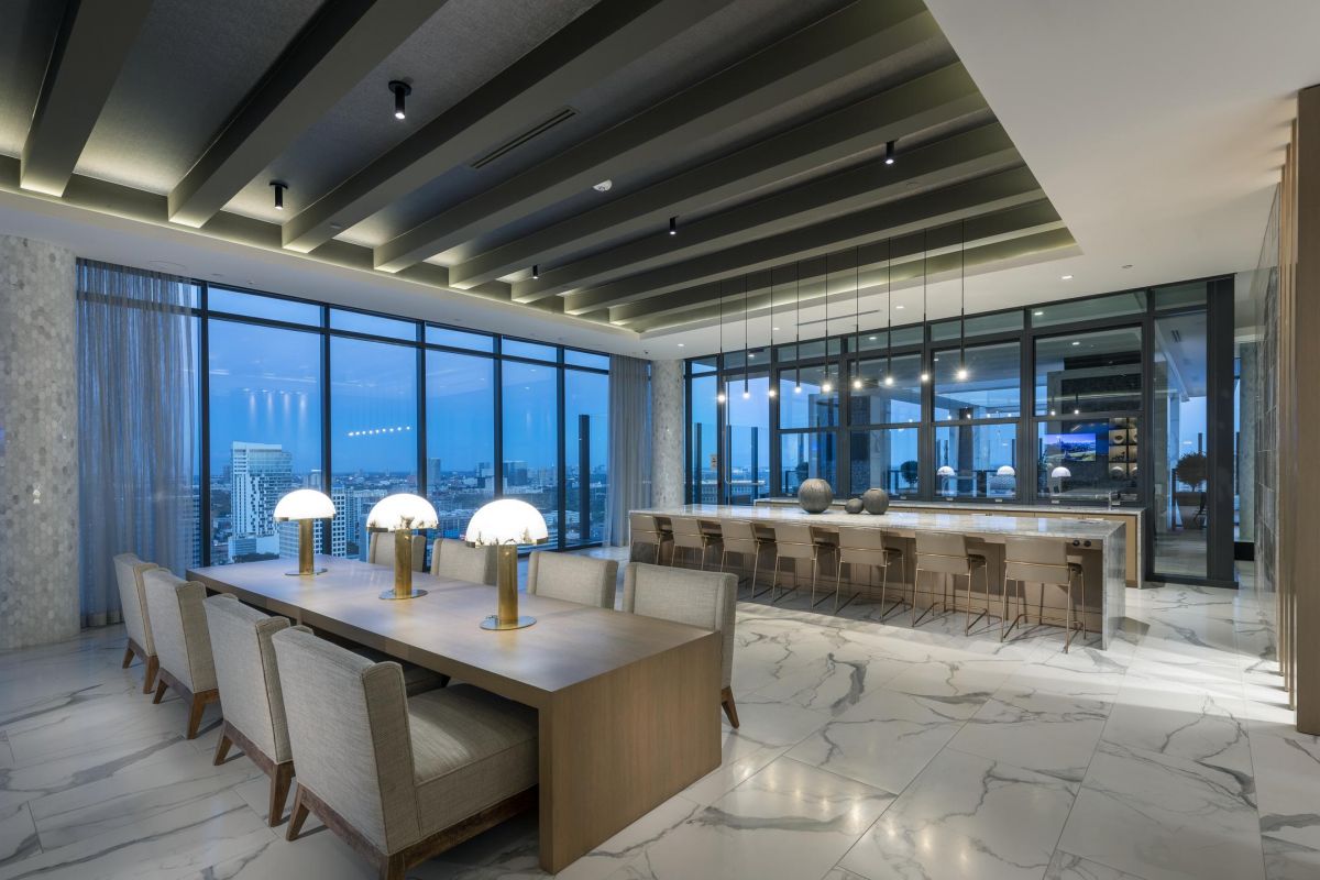 Luxurious dining area with a long table, stylish lighting, and large windows overlooking a city skyline.