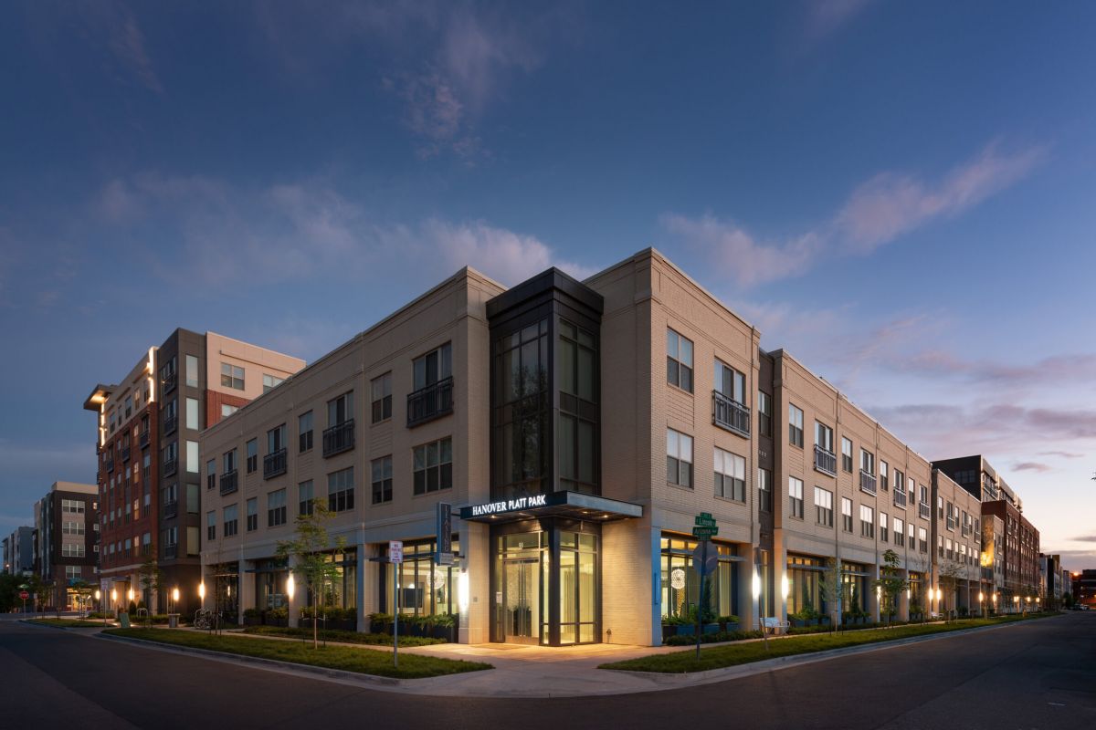 Modern apartment building at dusk with illuminated windows and a corner entrance on a quiet street.