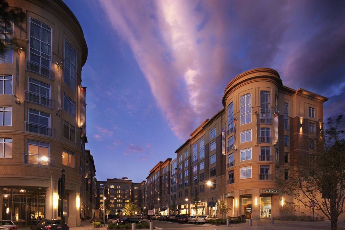 Modern apartment buildings line a street at dusk, beneath a dramatic, colorful sky with scattered clouds.