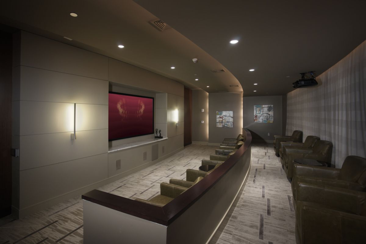 Modern home theater room in Charles River Landing apartment with recliner chairs, large screen, wall lights, and carpeted floor.