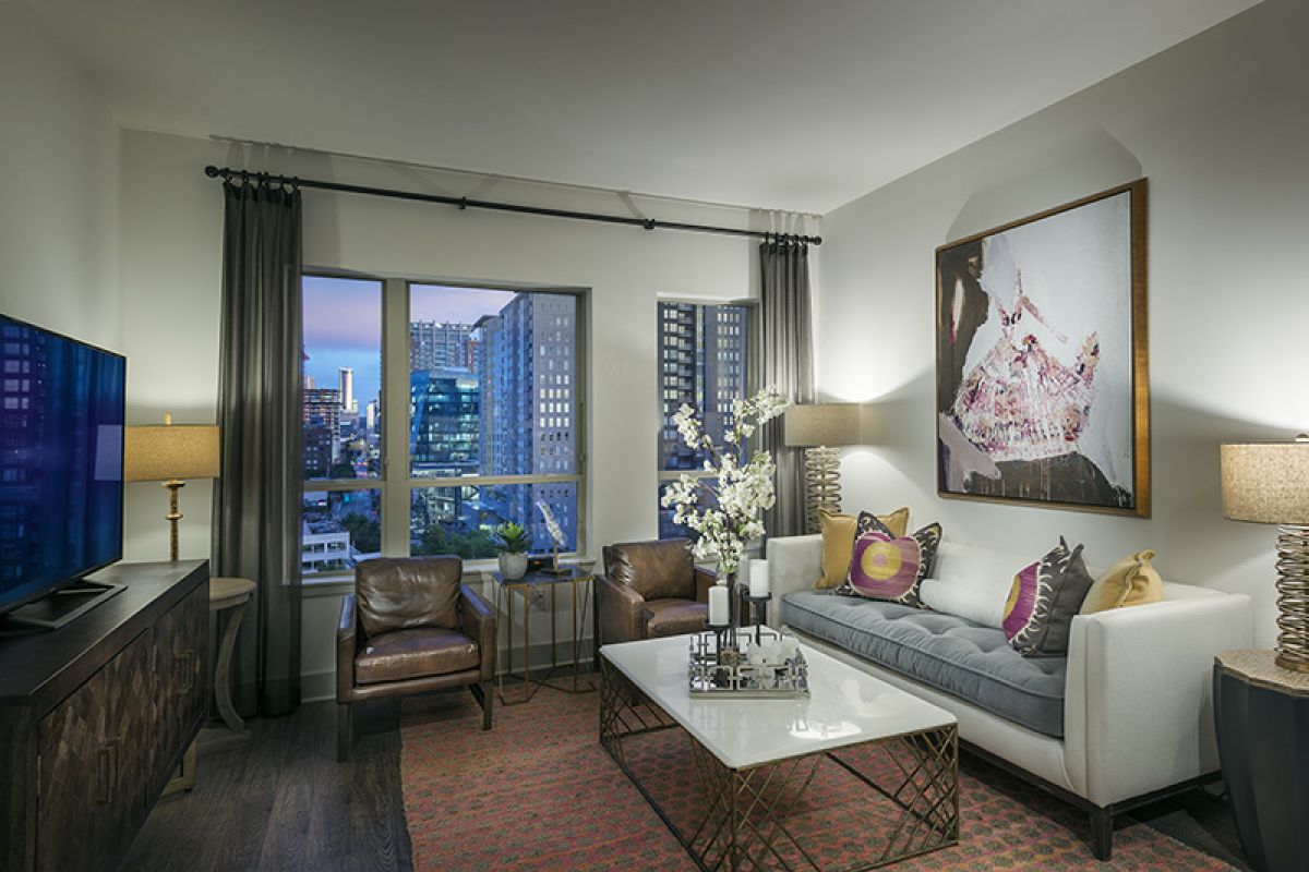 Modern living room with city view, gray sofa, two brown chairs, lamps, and contemporary decor.