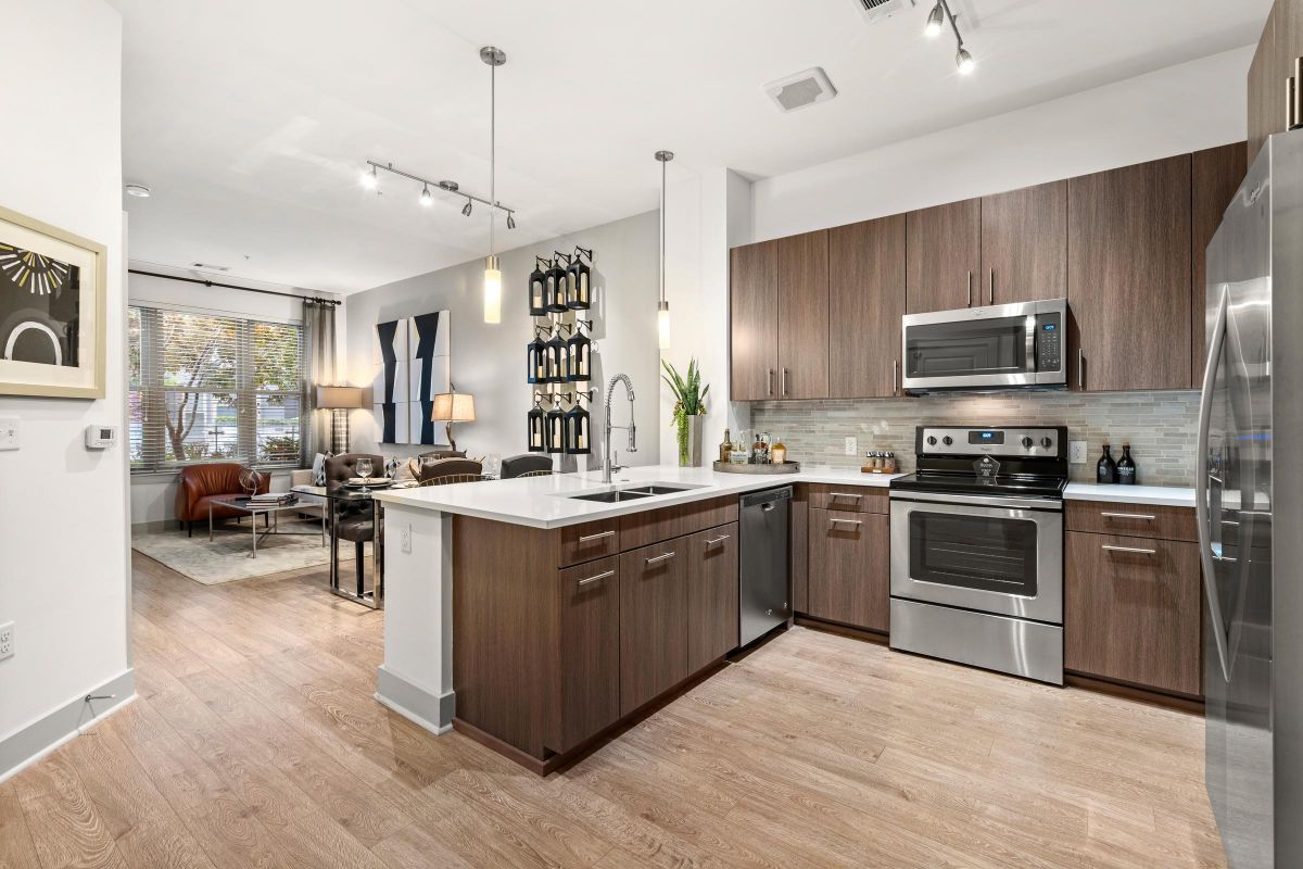 Modern open-concept kitchen and living area with wood cabinets, stainless steel appliances, and light wood flooring.