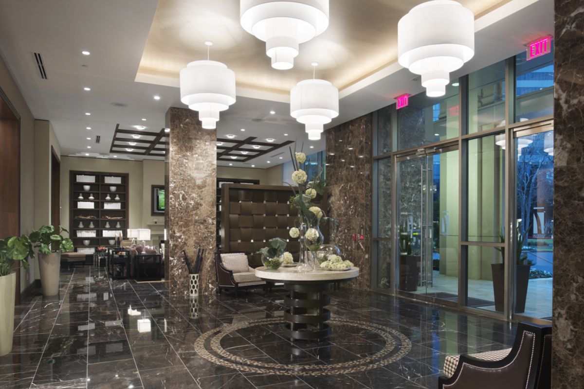 Modern hotel lobby with marble floors, large chandeliers, and elegant seating near glass entrance doors.