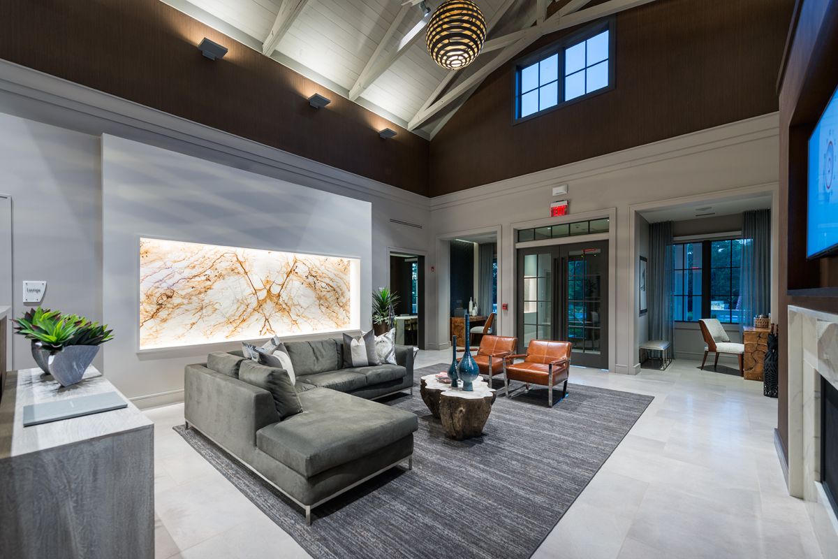 Modern lobby with a gray sectional sofa, two brown chairs, and a marble accent wall under high ceilings.