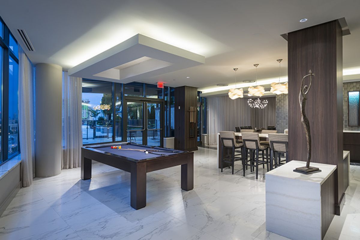 Modern lounge with a pool table, bar seating, large windows, and contemporary décor in a bright, open space.
