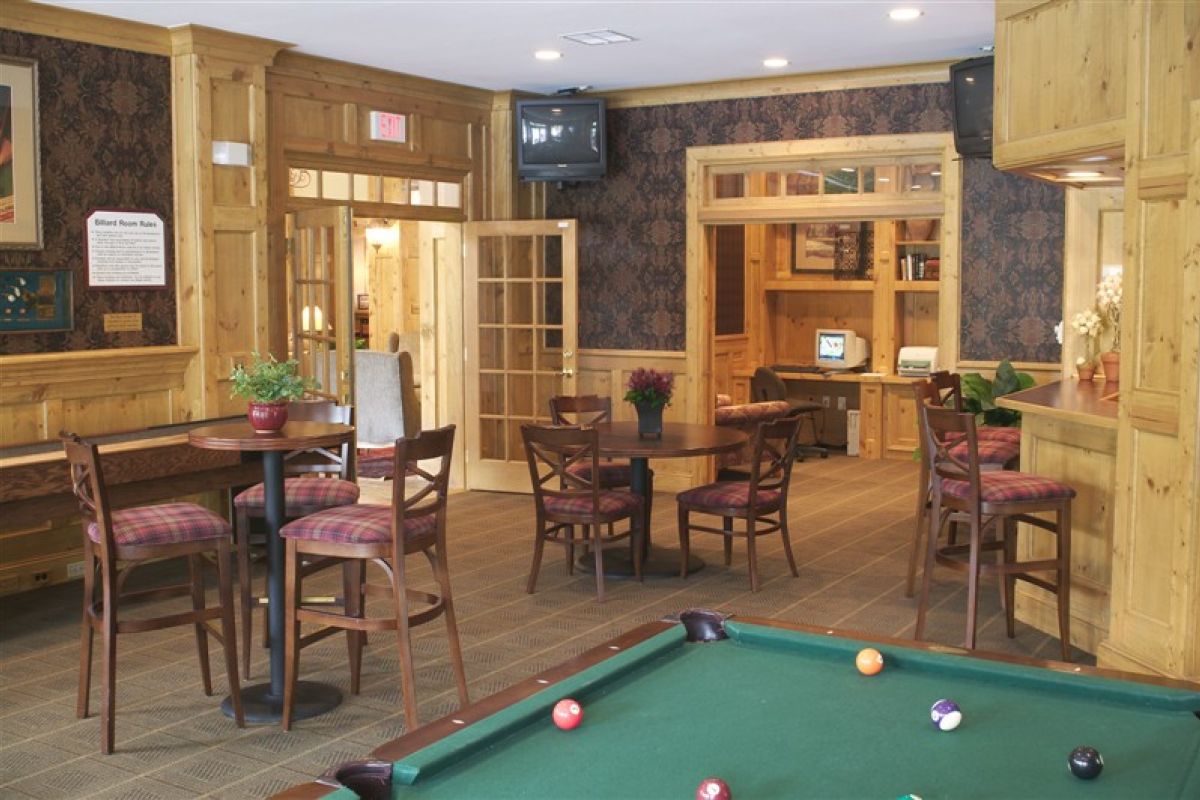 A cozy game room with wooden furniture, tables, chairs, and a pool table with balls.