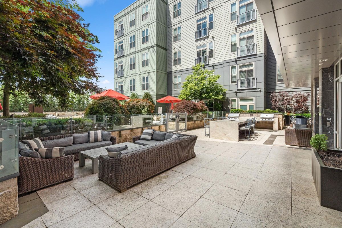 Outdoor patio with wicker furniture, dining area, red umbrellas, and potted plants near a modern building.