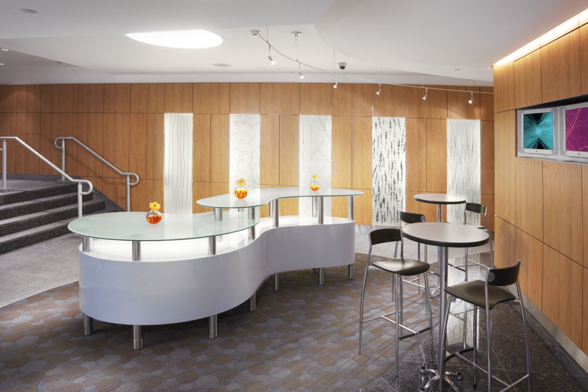 Modern lounge area with curved glass tables, bar stools, wood-paneled walls, and decorative vases.