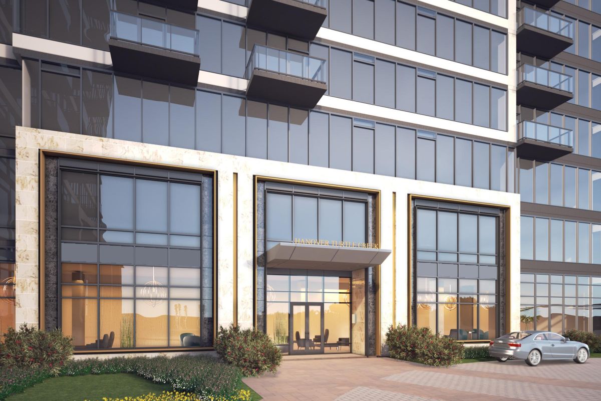 Modern building entrance with large windows, decorative plants, and a parked car in front.