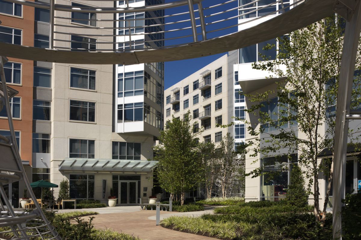 Curved walkway through a landscaped courtyard surrounded by modern apartment buildings and metal structures.