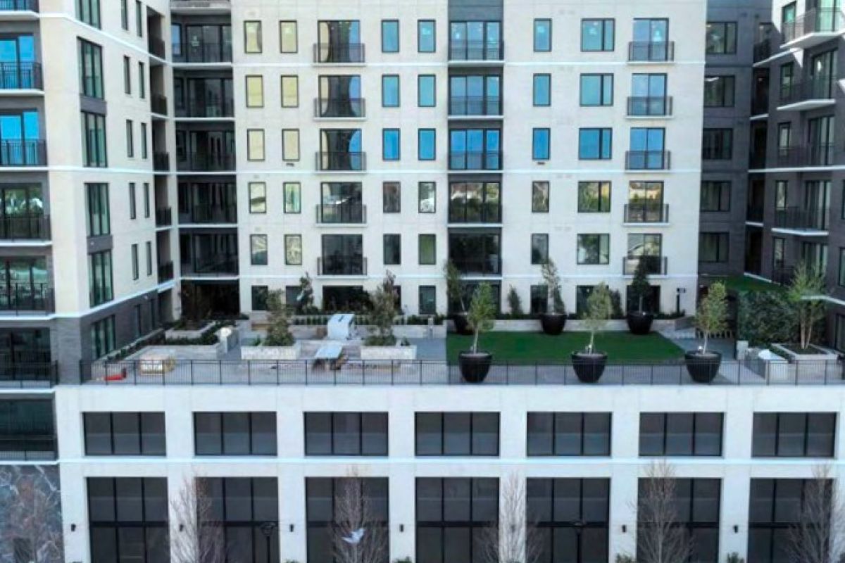 Modern apartment building with balconies and a landscaped terrace featuring large planters and seating areas.