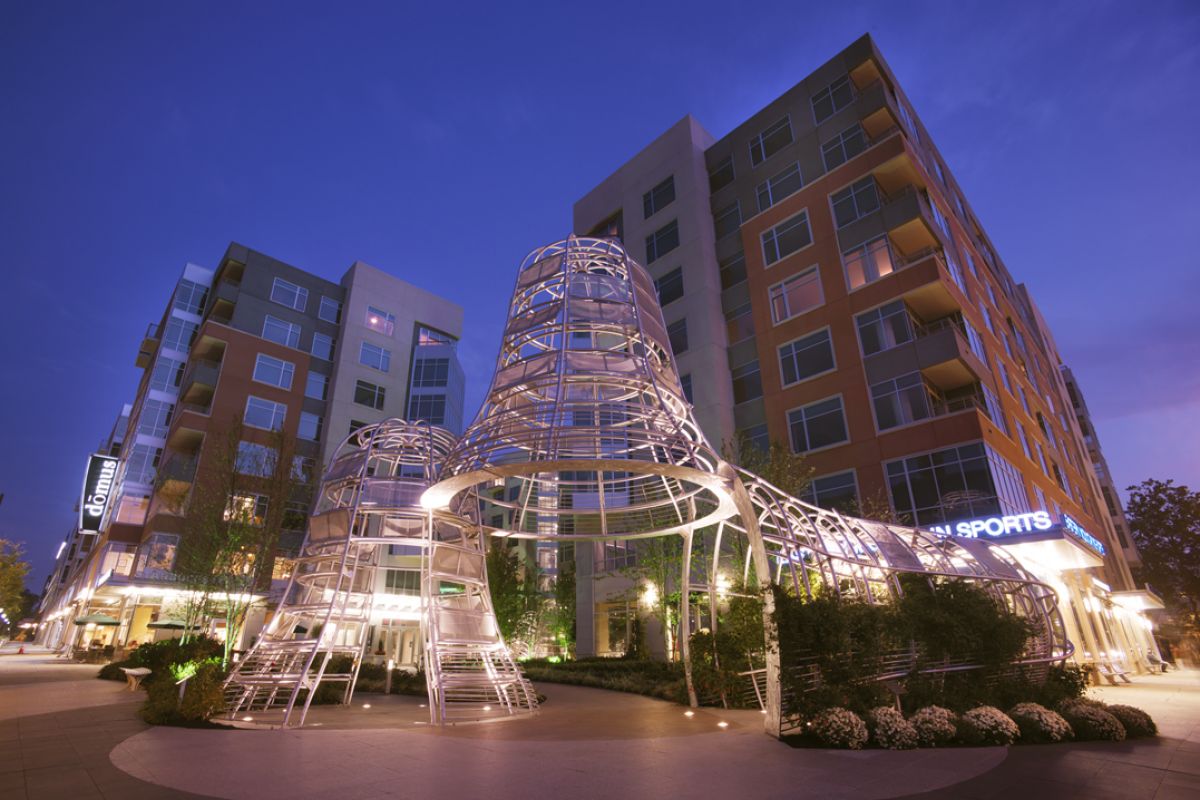 Modern apartment buildings at dusk with a large, artistic metal sculpture in the foreground.