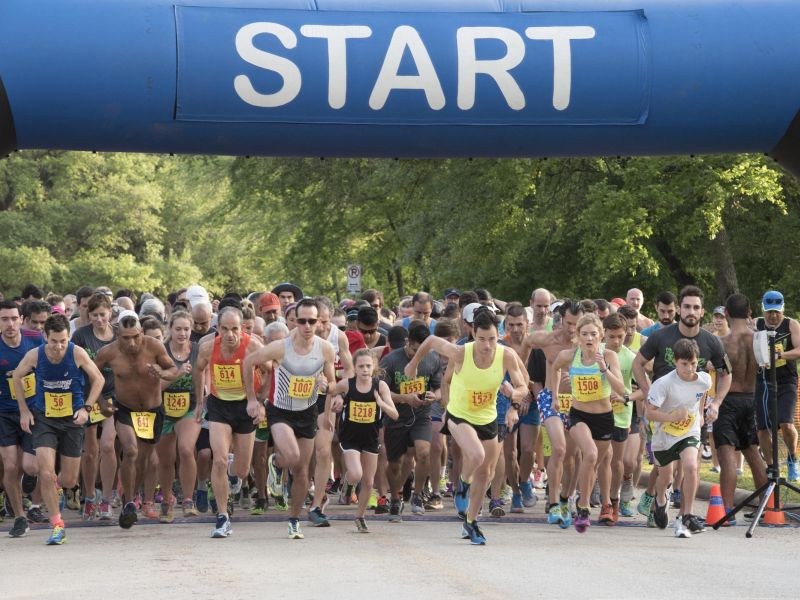 A large group of runners start a race under an inflatable arch that says "START.