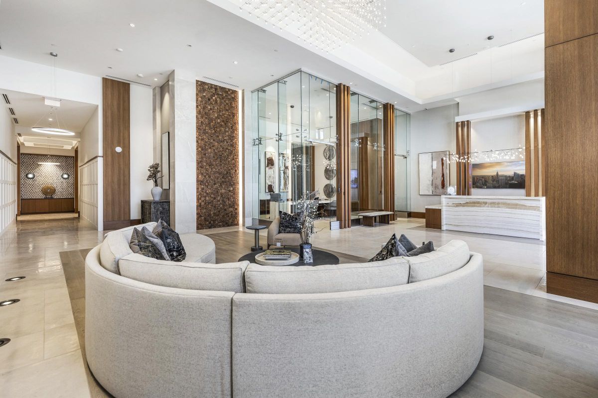 Modern hotel lobby with a round sofa, decorative pillows, wooden accents, and a reception desk in the background.