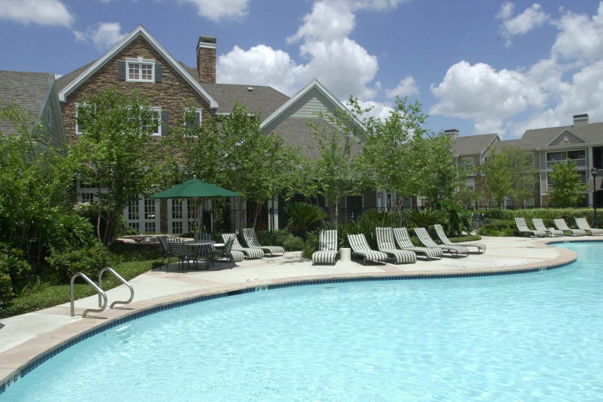 Outdoor swimming pool with lounge chairs and a green umbrella at Churchill on the Park apartments in Dallas on a sunny day.
