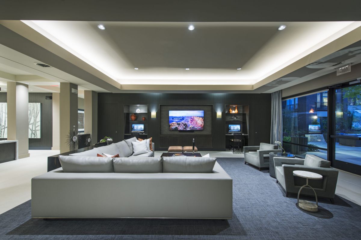 Modern lounge with a white sectional sofa, armchairs, TV, and large windows letting in natural light.