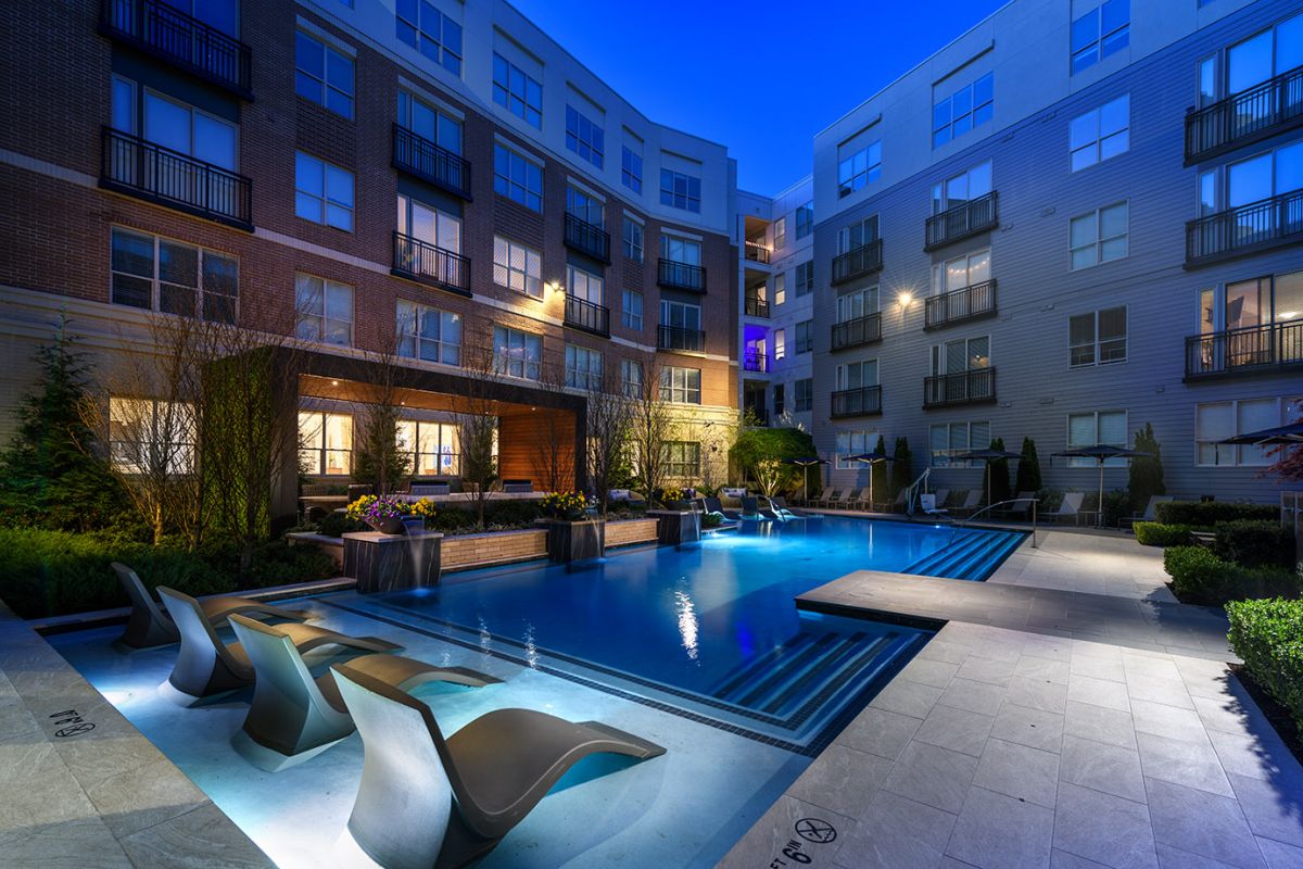 Modern apartment courtyard at dusk with a lit swimming pool and lounge chairs, showcasing luxury apartments at Hanover Exton Square.