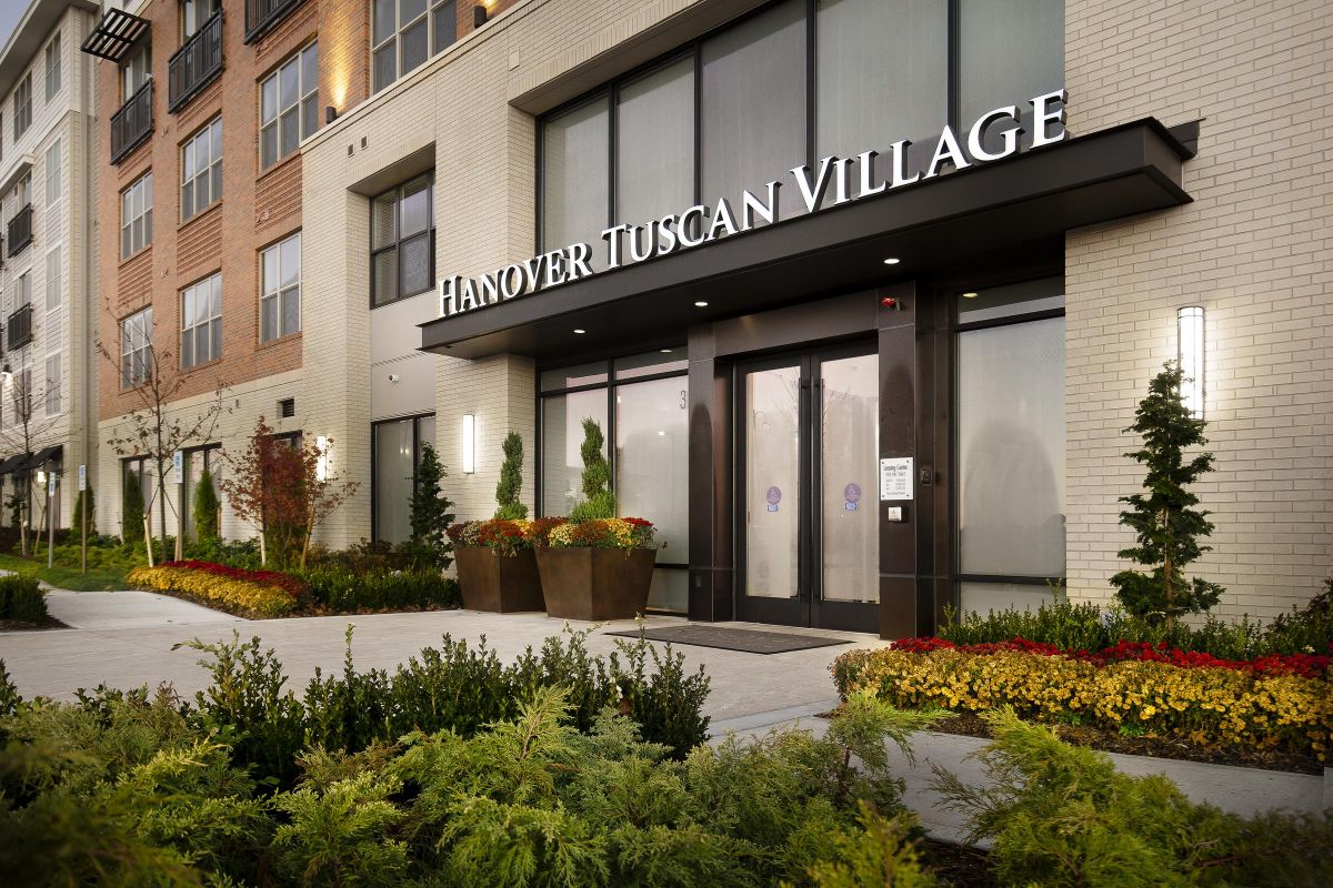 Entrance of Hanover Tuscan Village with modern glass doors, potted plants, and landscaped greenery.