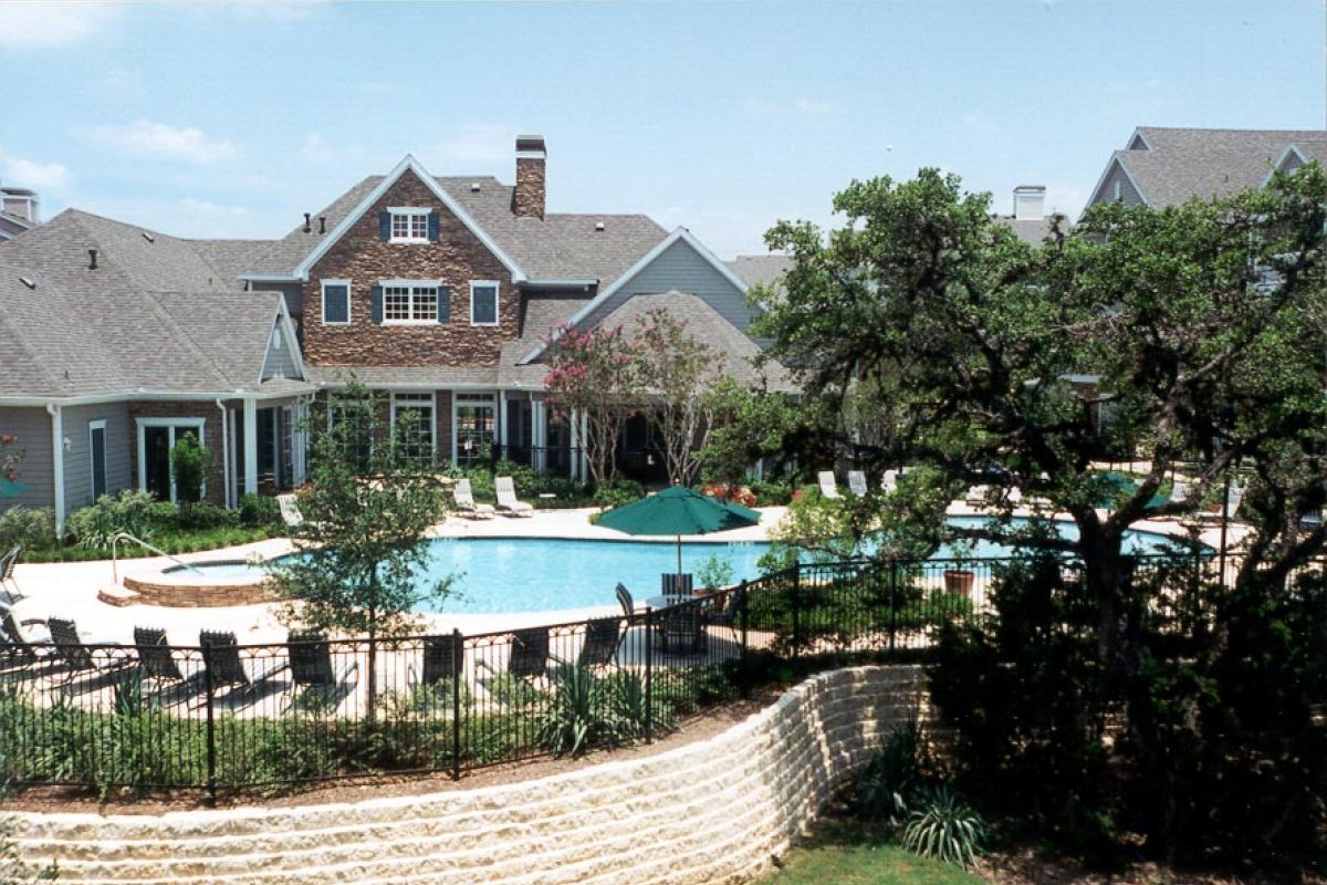 Large house with a fenced outdoor pool, loungers, and trees in a landscaped yard on a sunny day.