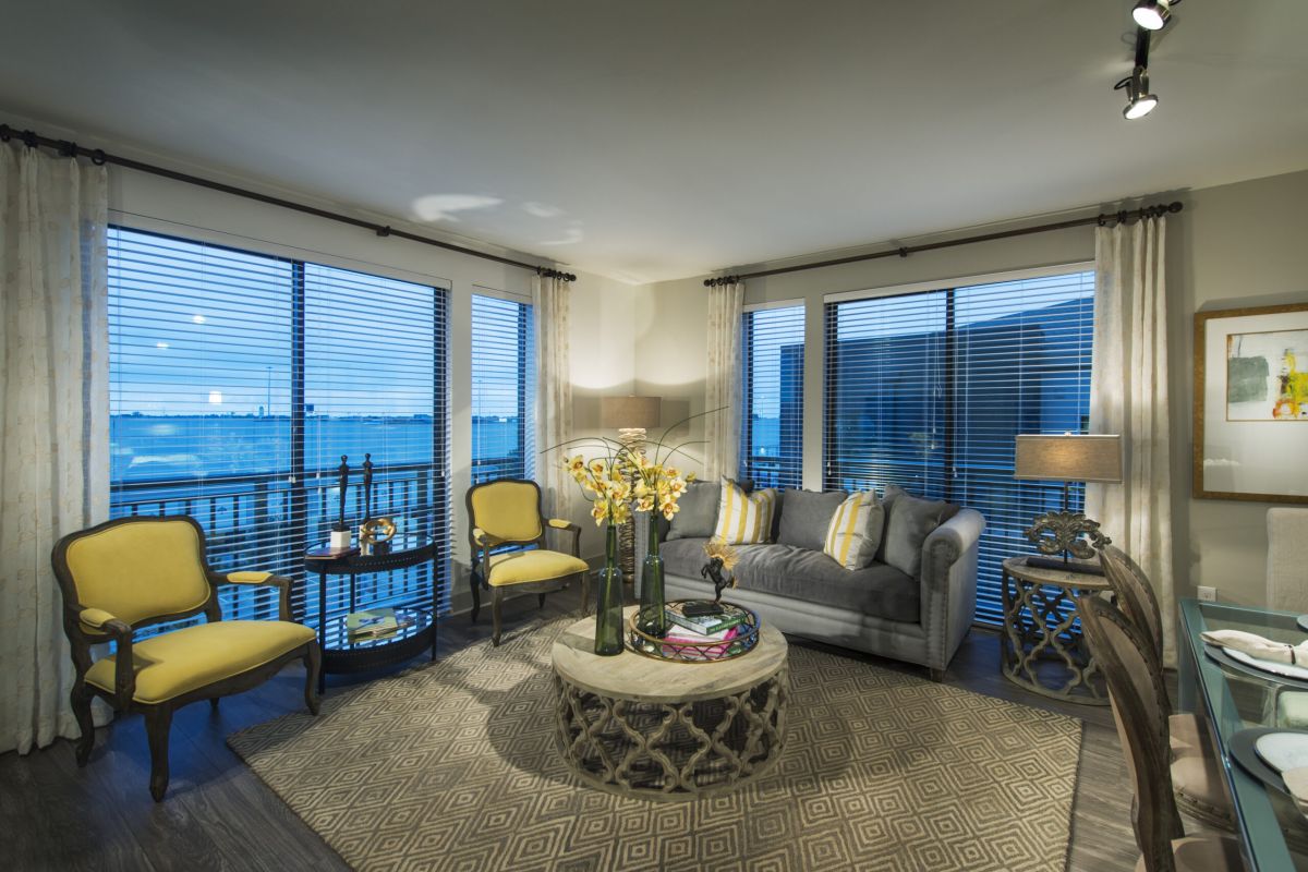 Modern living room with large windows, yellow chairs, gray sofa, and round coffee table with flowers.