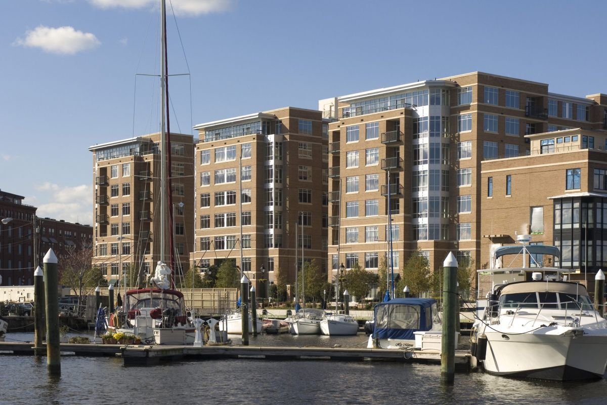 Boats docked at a marina in front of modern brick apartment buildings on a sunny day.