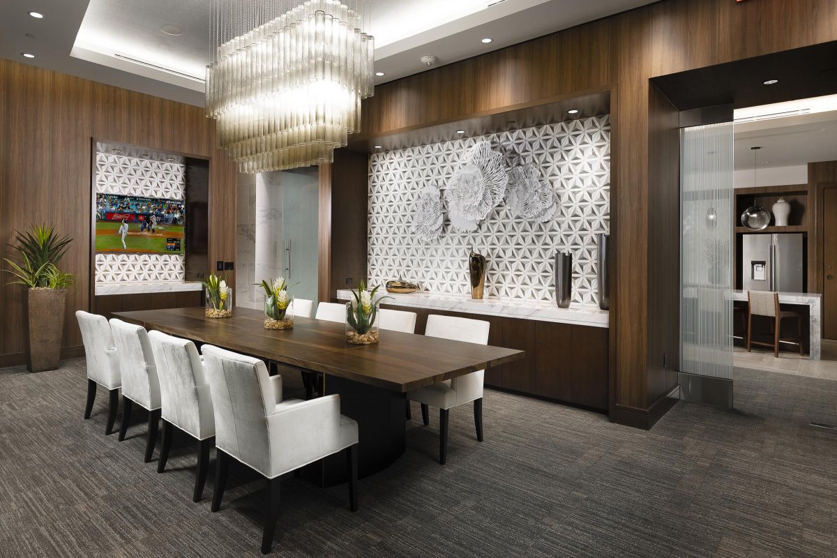 Modern dining room with a long wooden table, white chairs, decorative wall paneling, and a TV displaying a sports game.