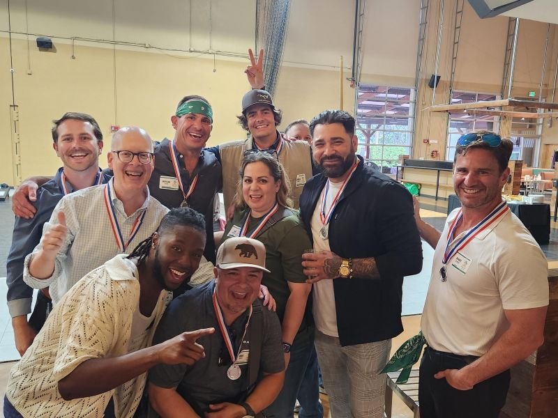 A group of people wearing medals pose together indoors, smiling and celebrating.