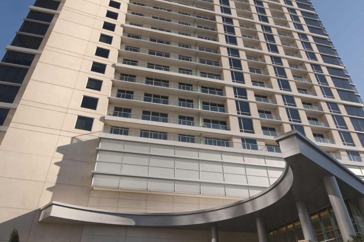 Tall modern hotel building with glass entrance, viewed from below against a clear blue sky.
