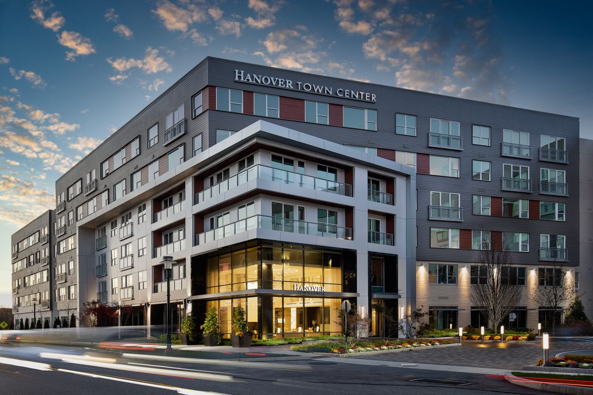 Modern multi-story building labeled “Hanover Town Center” with large windows, balconies, and evening lighting.