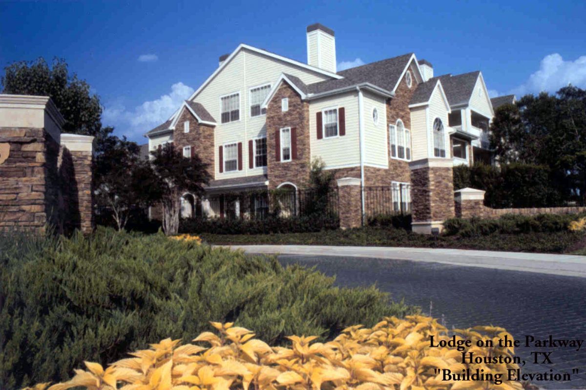 Large multi-story lodge with stone and siding exterior at Broadwater Galveston, surrounded by greenery and yellow plants under a blue sky.