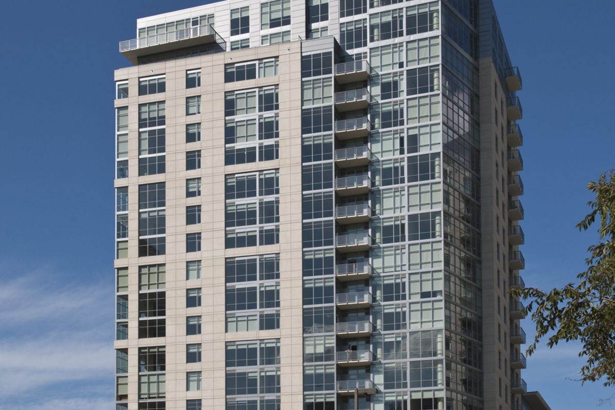 Modern high-rise apartment building with glass and concrete facade under a clear blue sky.