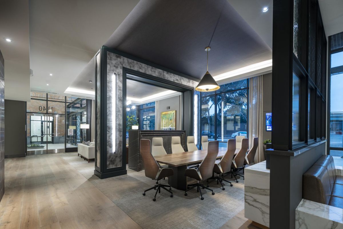 Modern office space with a long wooden table, brown chairs, pendant light, and large windows.