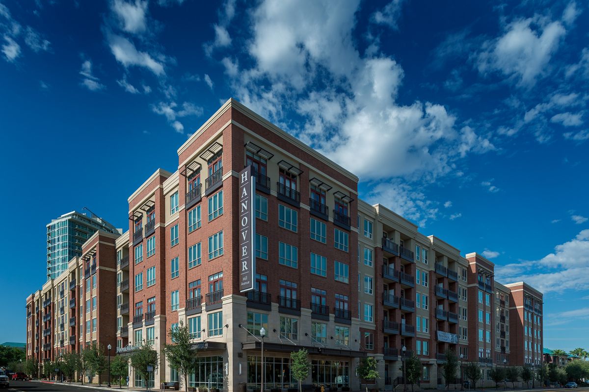 A modern, multi-story brick apartment building under a bright blue sky with scattered clouds.