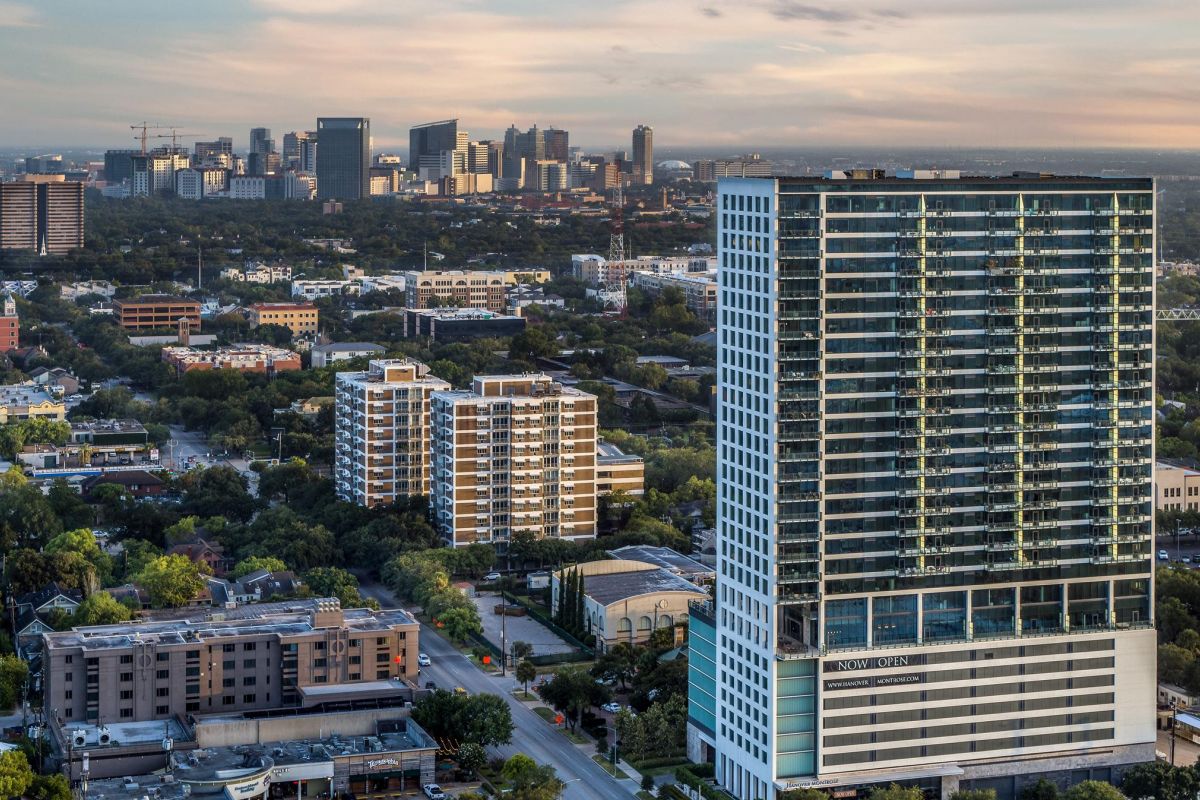 Aerial view of a cityscape with a tall, modern building in the foreground and a distant skyline at sunset.