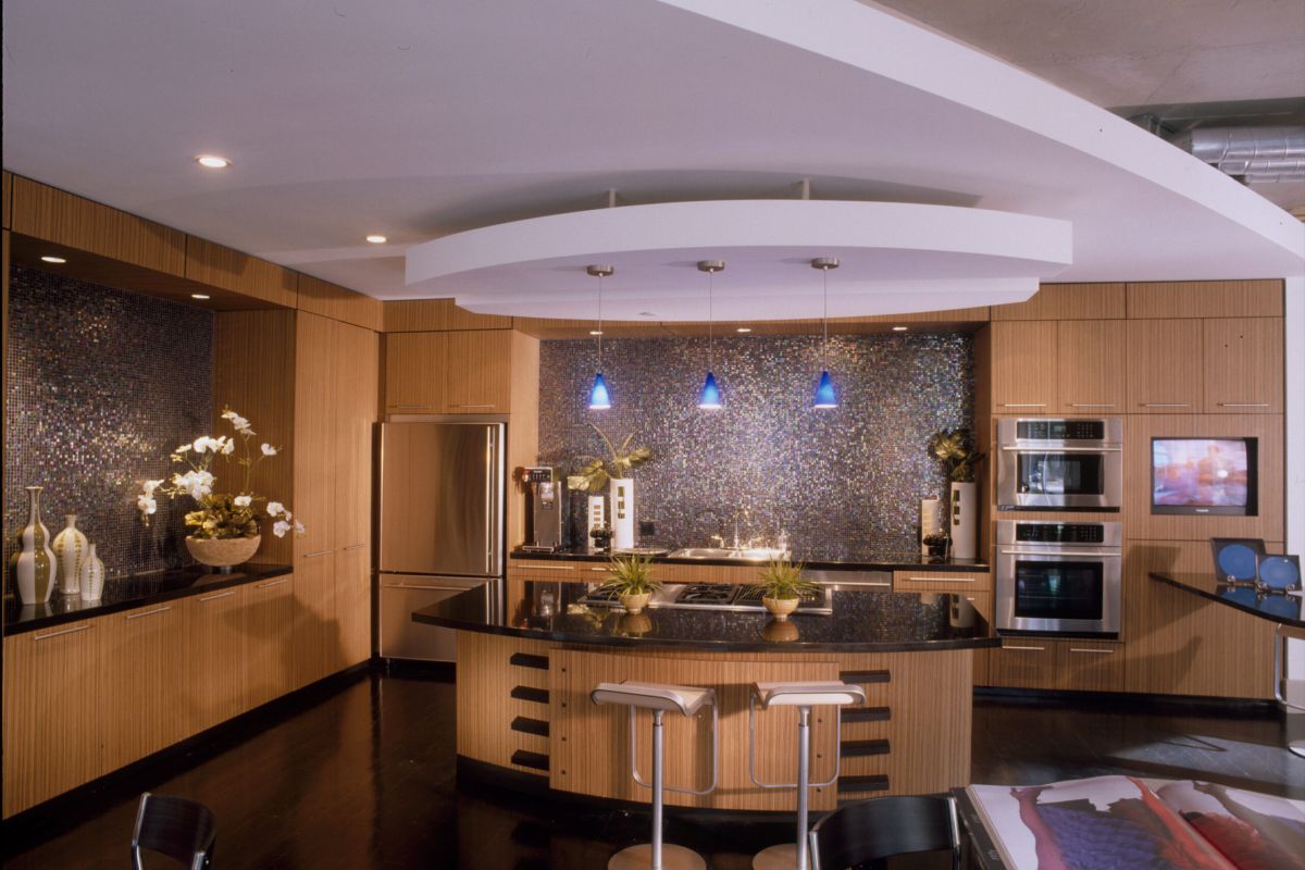 Modern kitchen with wood cabinets, black countertops, an island, and blue pendant lights.