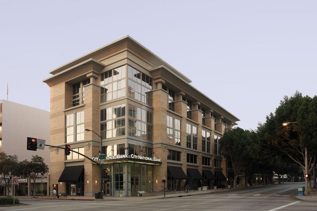 A modern, multi-story building with "City National Bank" signage on a quiet street corner in the early morning.