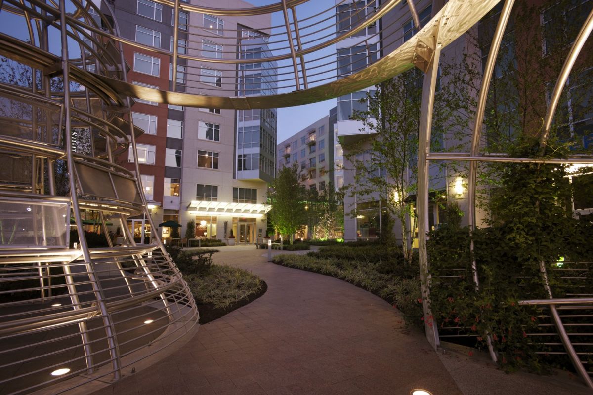 Curved walkway through a modern apartment courtyard with metal and glass architectural structures at dusk.