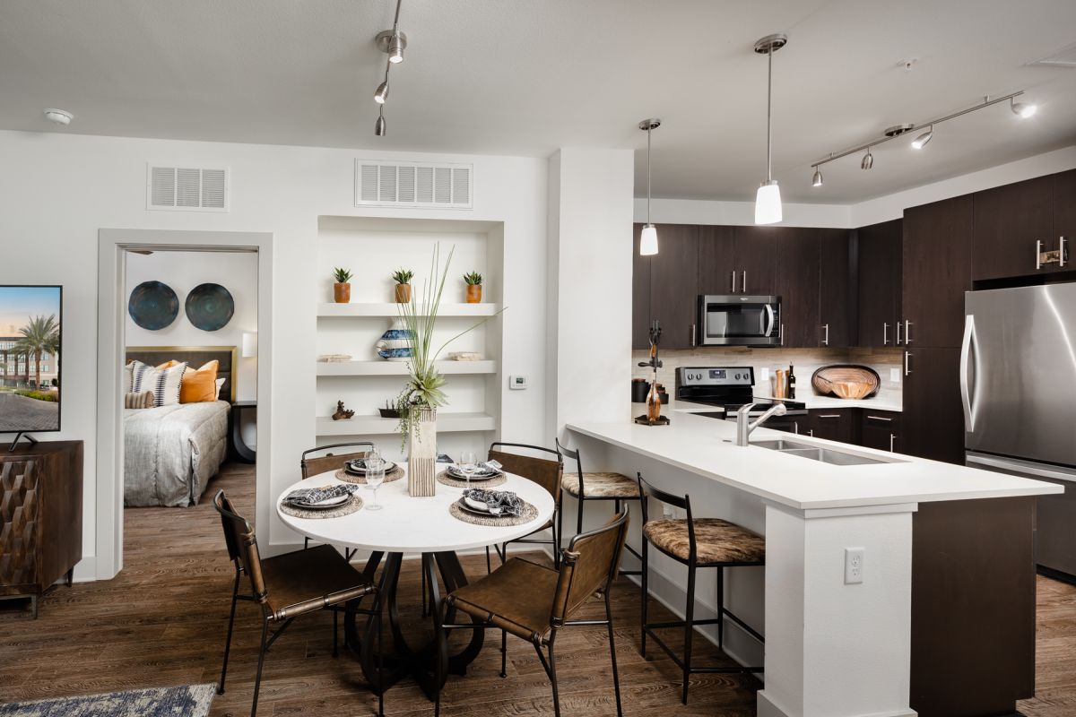 Modern kitchen and dining area with dark cabinets, open shelves, set table, and view into bedroom.