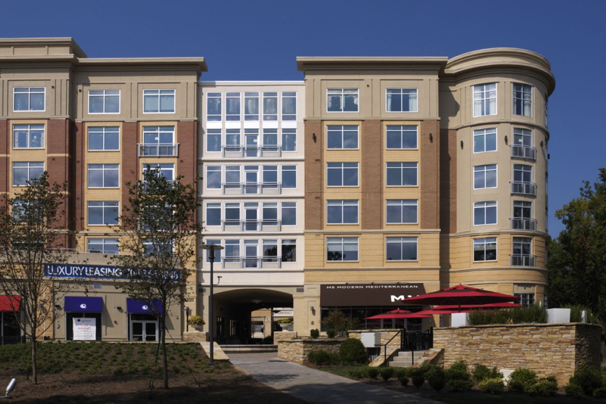 Modern apartment building with large windows, restaurant patio, and leasing office under a clear blue sky.