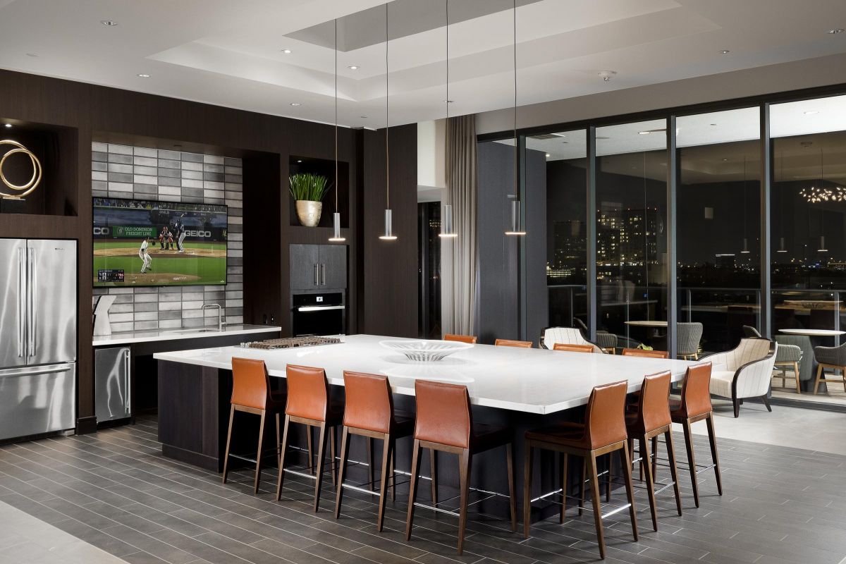 Modern kitchen with a large island, leather chairs, pendant lights, and a wall-mounted TV showing a baseball game.