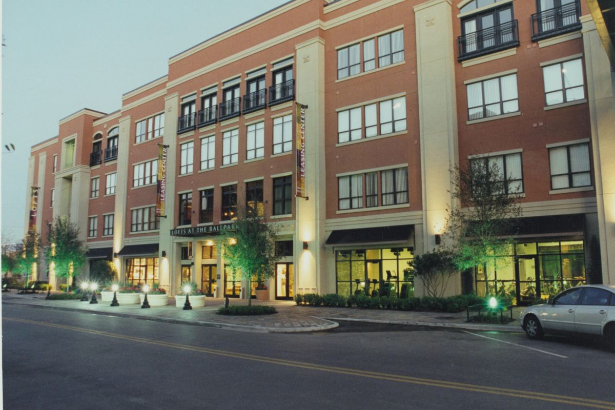 Four-story modern building with shops at street level, large windows, and cars parked along the road at dusk.