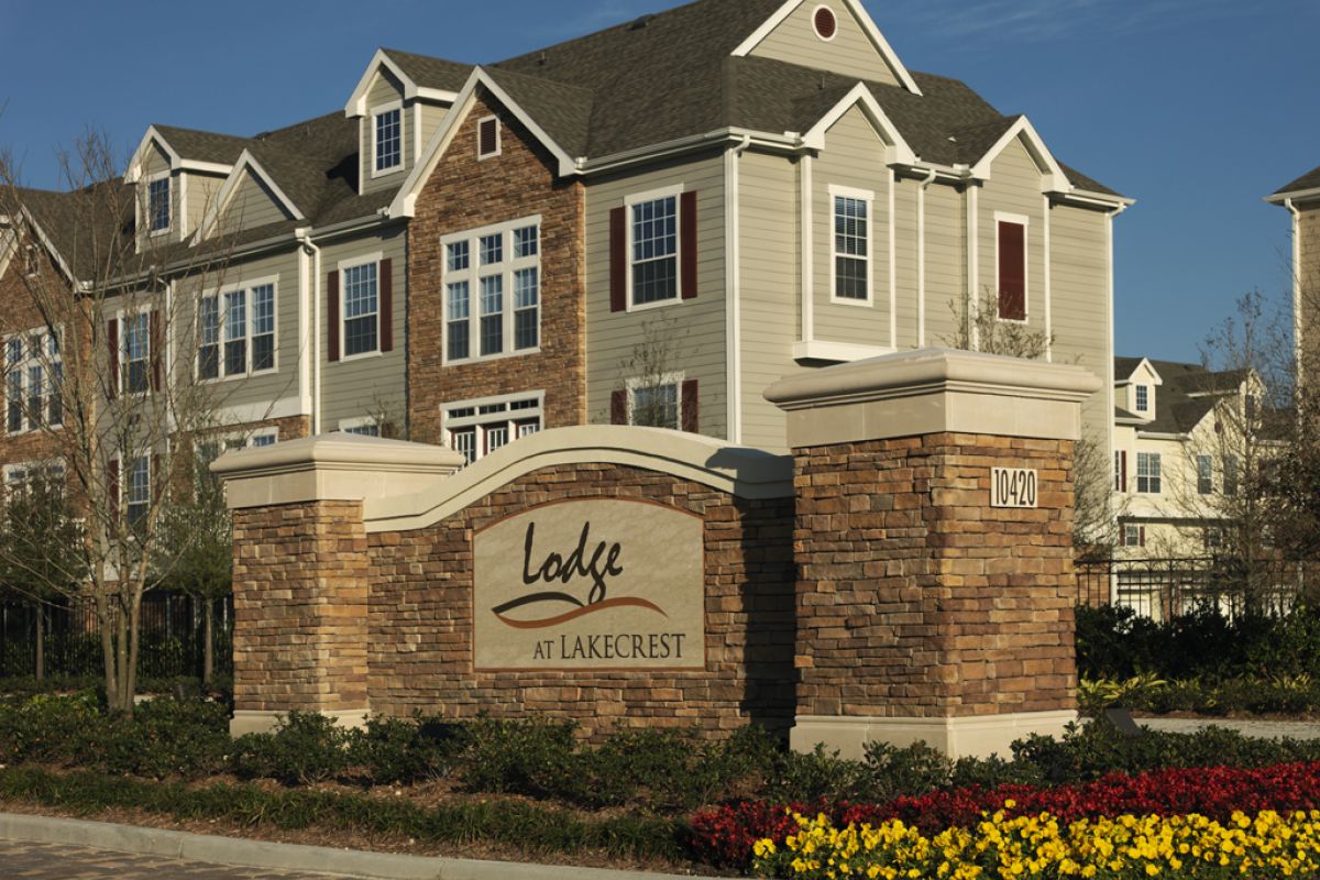 Apartment complex with "Lodge at Lakecrest" sign, brick entrance, and landscaped flowers in front.