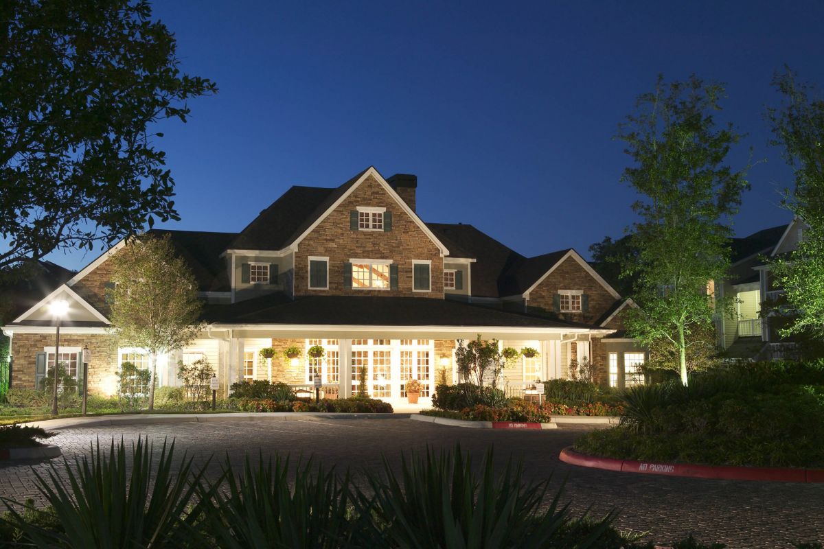 A large, well-lit house with a brick exterior and manicured landscaping at dusk.